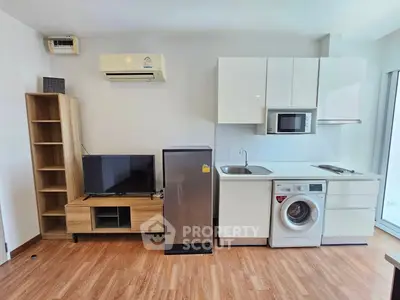 Modern studio apartment with compact kitchen and appliances, featuring a washing machine and microwave.