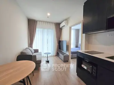 Modern living room with open kitchen, featuring sleek furniture and natural light.