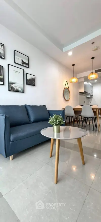 Modern living room with stylish decor and open kitchen layout, featuring a cozy blue sofa and elegant dining area.