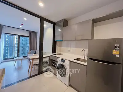 Modern open-layout kitchen with washing machine and fridge, leading to a bright living room with city view.