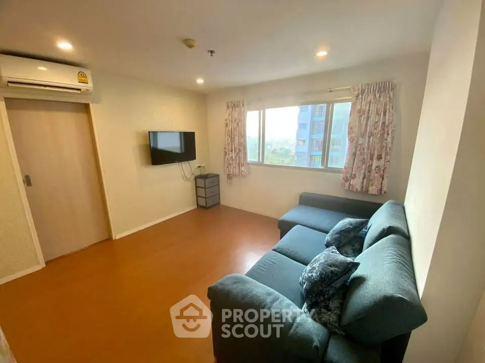 Cozy living room with modern sofa and wall-mounted TV, featuring natural light from large window.