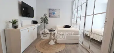 Modern living room with stylish decor and large windows, featuring a cozy white sofa and sleek TV setup.