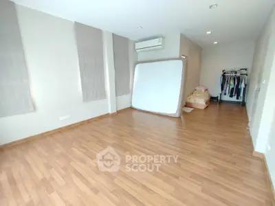 Spacious bedroom with wooden flooring and air conditioning, featuring a mattress and clothing rack.