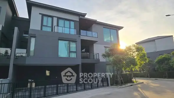 Modern three-story building with large windows and balconies at sunset.