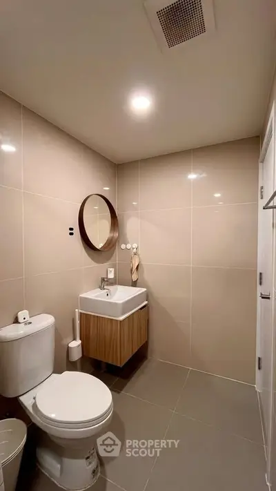 Modern bathroom with sleek fixtures and neutral tiles, featuring a round mirror and compact vanity.