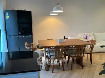 Modern dining area with wooden table and chairs, adjacent to a sleek black refrigerator and cozy living space.