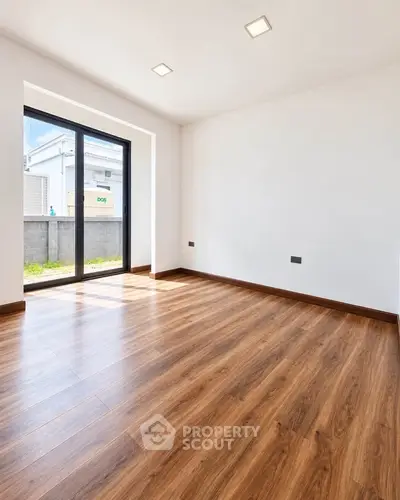 Spacious empty room with wooden flooring and large window, perfect for customization.