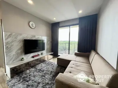 Spacious living room with modern marble TV wall, plush sofa, and balcony access offering natural light and a serene view, perfect for relaxation and entertainment.