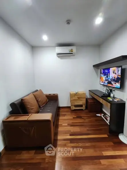 Cozy living room with modern furniture and wooden flooring, featuring a mounted TV and air conditioning.