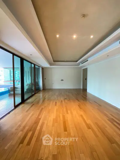 Spacious empty living room with wooden flooring and large glass doors leading to balcony.