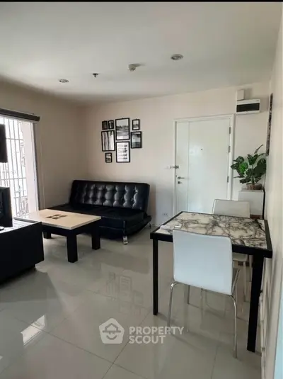 Modern living room with sleek black sofa and marble dining table in a bright apartment.