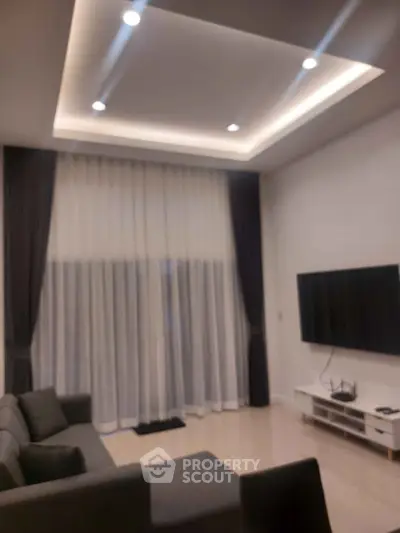 Modern living room with sleek design, featuring a large TV and elegant curtains.