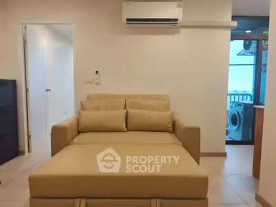 Cozy living room with beige sofa and air conditioning, featuring a view into a laundry area with washing machine.