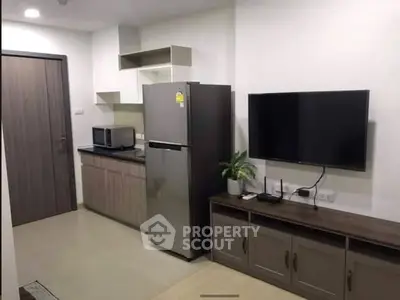 Modern apartment interior with kitchen and living area featuring fridge and TV setup.