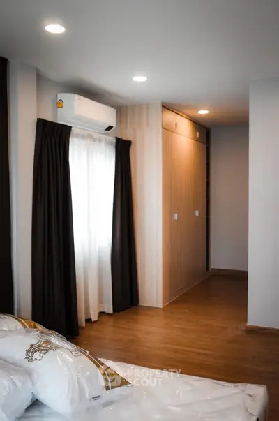 Modern bedroom with wooden flooring, built-in wardrobe, and natural light from window.