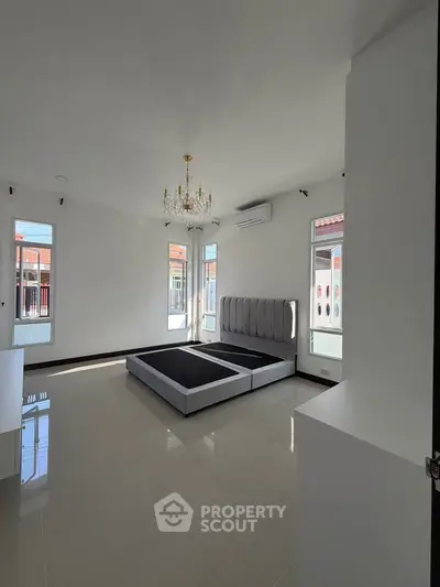 Spacious bedroom with elegant chandelier and modern bed frame, ample natural light from large windows.