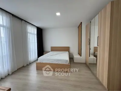 Spacious modern bedroom with large windows and wooden furniture, perfect for natural light lovers.
