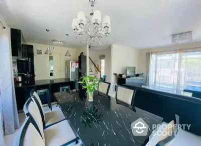 Elegant dining area with modern chandelier and sleek black table in open-plan living space.