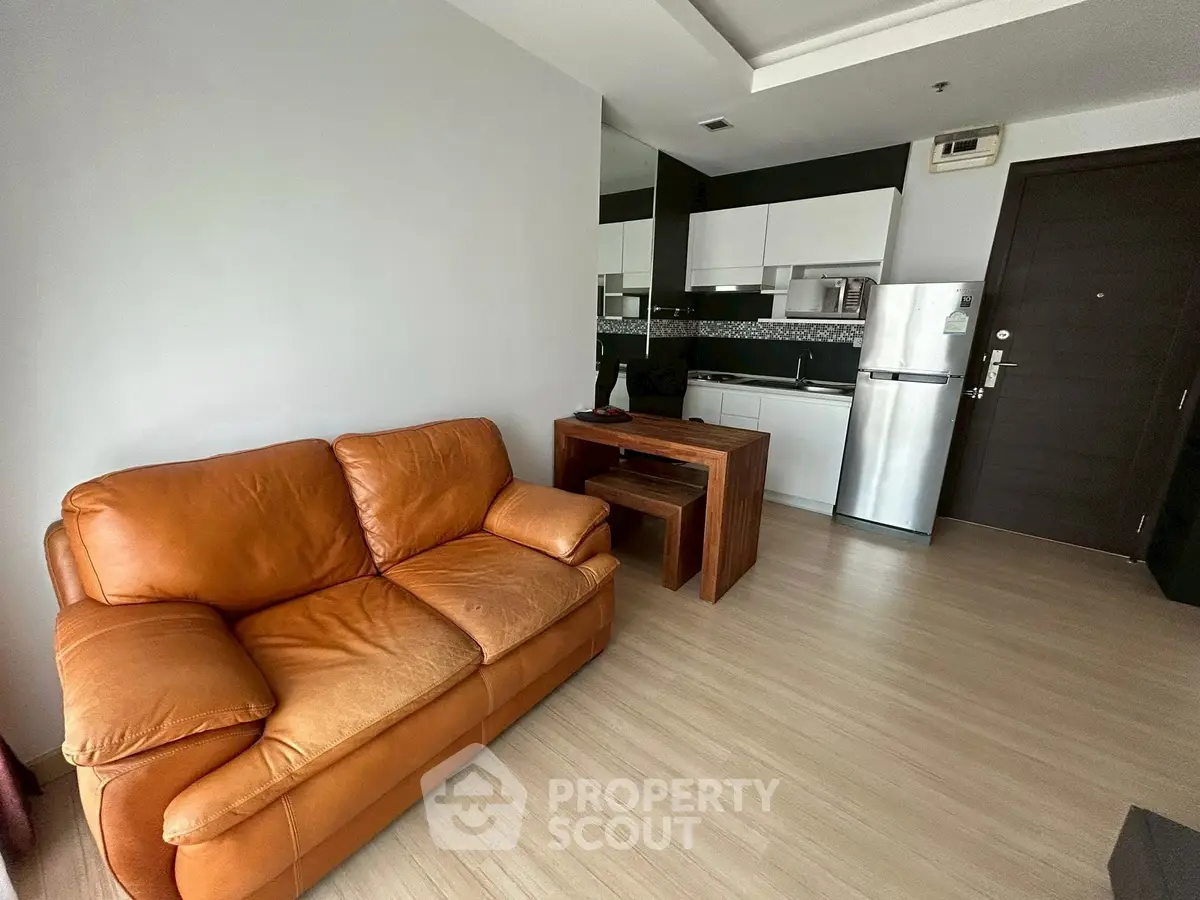 Modern apartment interior with cozy leather sofa and compact kitchen area.