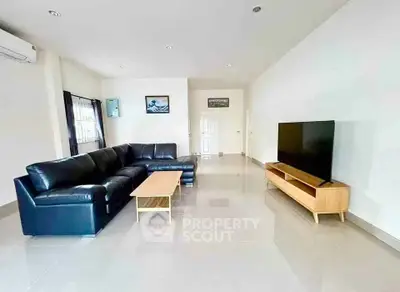 Spacious modern living room with sleek black leather sofa and large flat-screen TV, perfect for relaxation.