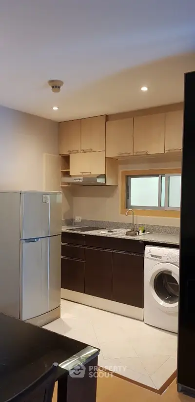 Modern kitchen with sleek cabinets, stainless steel fridge, and washing machine.