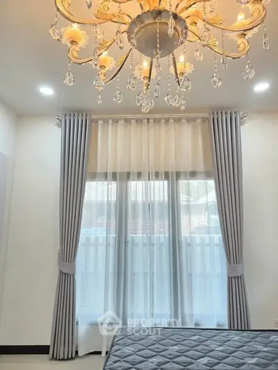 Elegant bedroom with chandelier and large window, featuring luxurious curtains and a stylish bed.