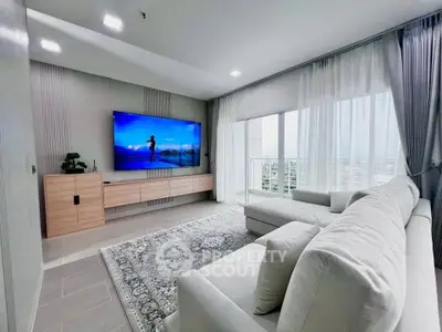 Modern living room with large TV and elegant sofa, featuring a stunning city view through floor-to-ceiling windows.
