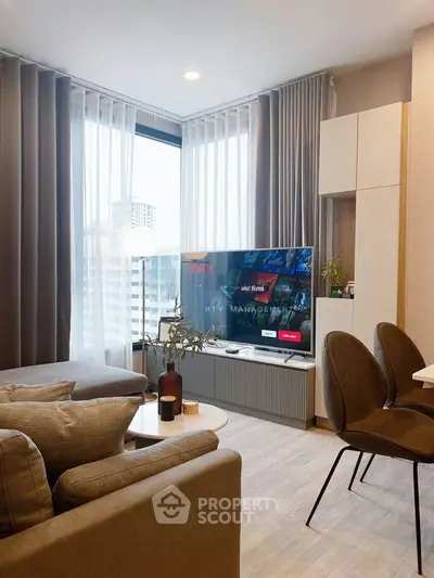Modern living room with large TV, stylish furniture, and city view through large windows.