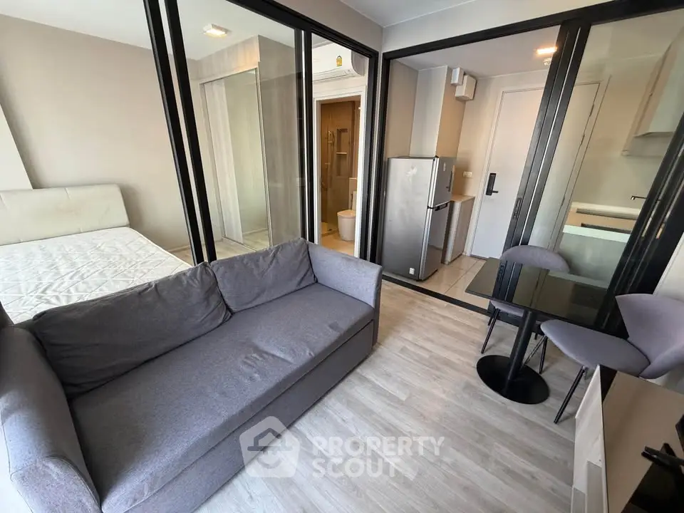 Modern studio apartment with glass partitions, cozy sofa, and compact kitchen area.