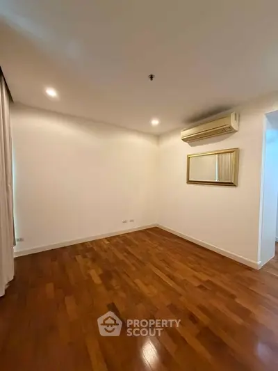 Spacious empty room with wooden flooring and air conditioning, ideal for customization.