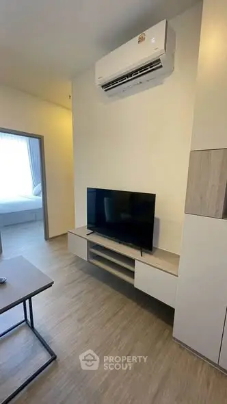 Modern living room with sleek TV setup and air conditioning, leading to a cozy bedroom.