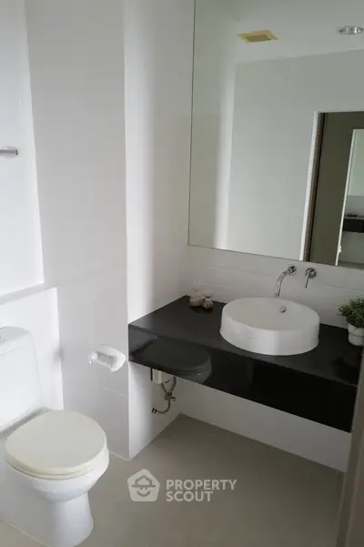 Modern bathroom with sleek design featuring a round basin and large mirror.