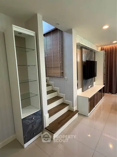 Modern living room with sleek staircase and built-in TV unit, featuring elegant design and ample natural light.