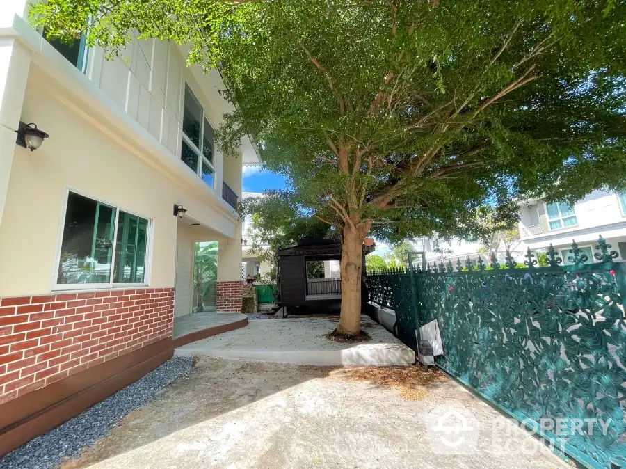 Charming suburban home exterior with a mature tree providing shade, a well-maintained garden, and a secure, decorative fence enhancing curb appeal.