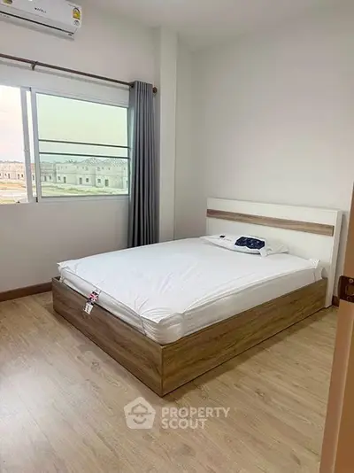 Modern minimalist bedroom with wooden flooring and large window view.