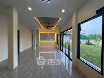 Spacious modern living room with large windows and garden view, featuring elegant ceiling lights and sleek flooring.