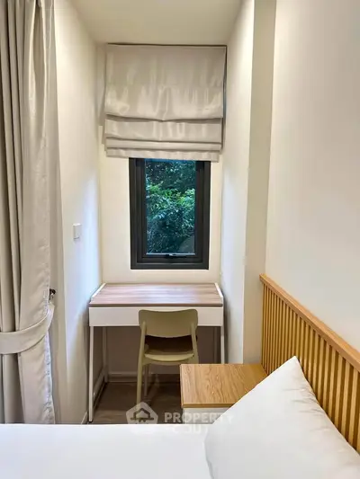 Cozy bedroom with a small study nook and window view of greenery, perfect for serene living.