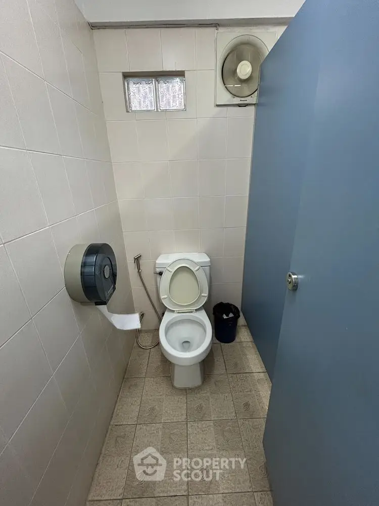 Compact bathroom with toilet and tiled floor, featuring a wall-mounted toilet paper holder.