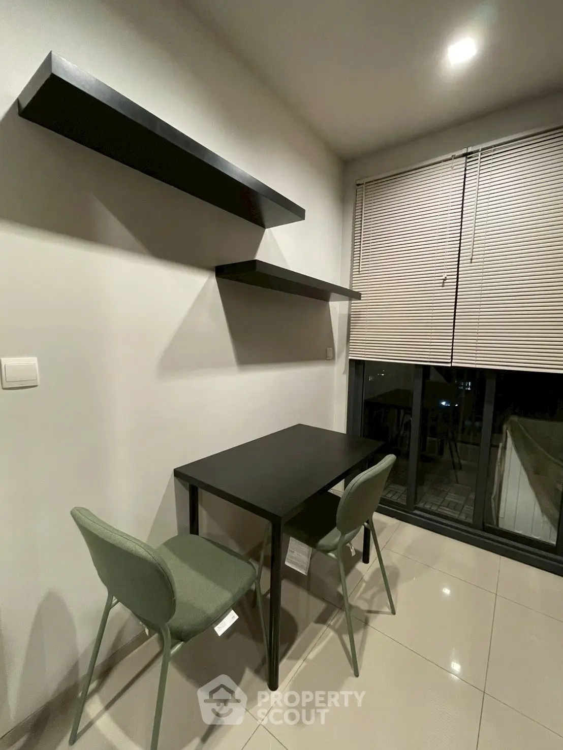 Modern study area with sleek black desk, chairs, and floating shelves in a well-lit room.