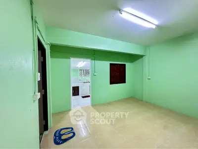 Spacious green-painted room with tiled flooring and bright lighting, ideal for versatile living space.