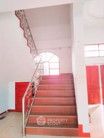 Elegant staircase with decorative railing in a bright interior space, featuring natural light and modern design.