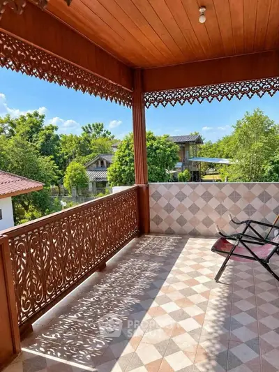 Charming wooden balcony with intricate railing and scenic view of lush greenery.