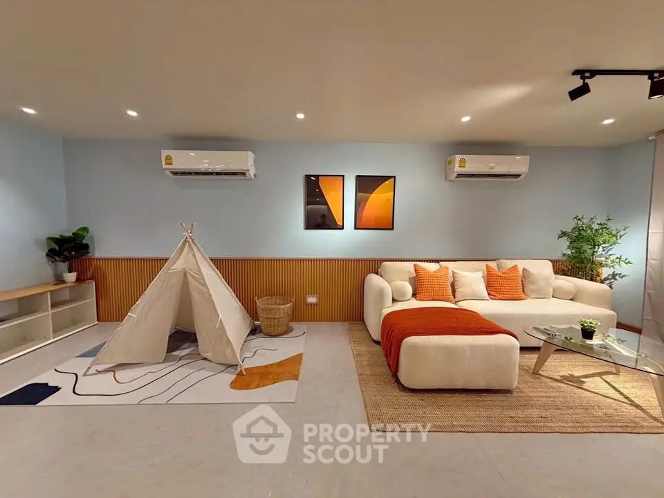 Spacious living room with modern decor, featuring a cozy sofa, stylish artwork, and a playful tent for kids.