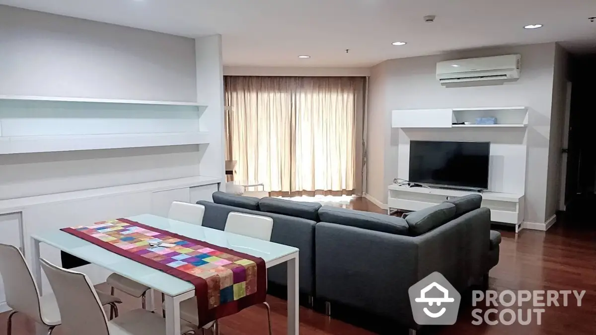 Spacious modern living room with sleek white entertainment unit, comfortable grey sofas, and a vibrant dining table set under warm lighting.