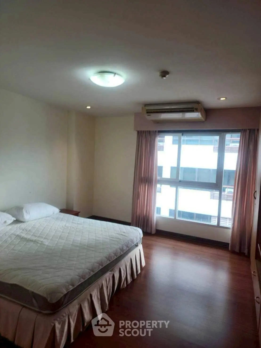 Spacious bedroom with large window and wooden flooring in modern apartment.