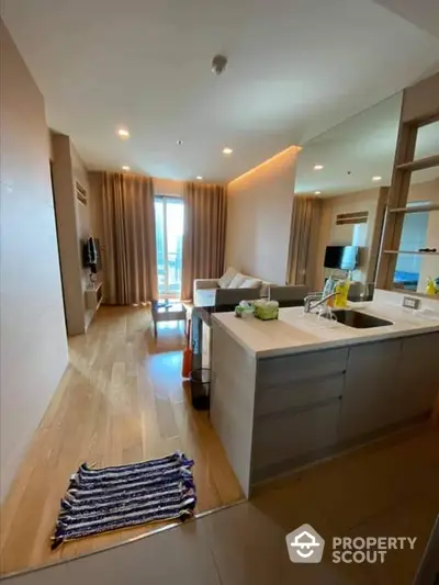 Modern open-plan kitchen with sleek countertops flows into a cozy living area, bathed in natural light from the balcony doors.