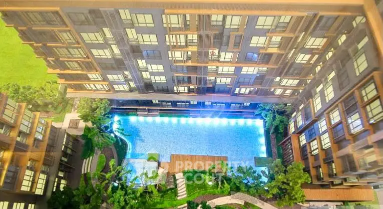 Stunning aerial view of modern apartment complex with illuminated pool and lush greenery.