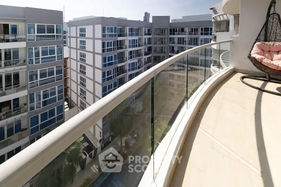 Luxurious balcony with glass railing offering stunning views of modern apartment buildings.