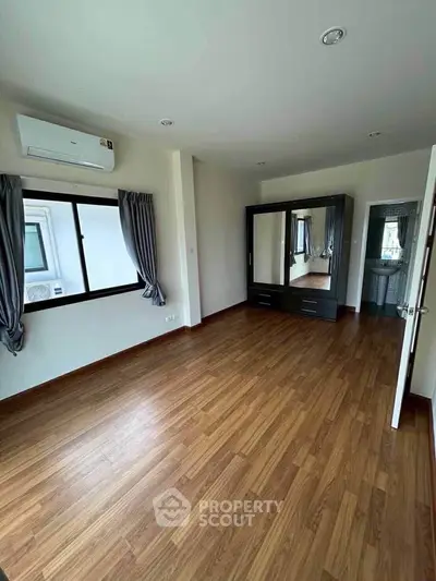 Spacious bedroom with wooden flooring and mirrored wardrobe in modern apartment.