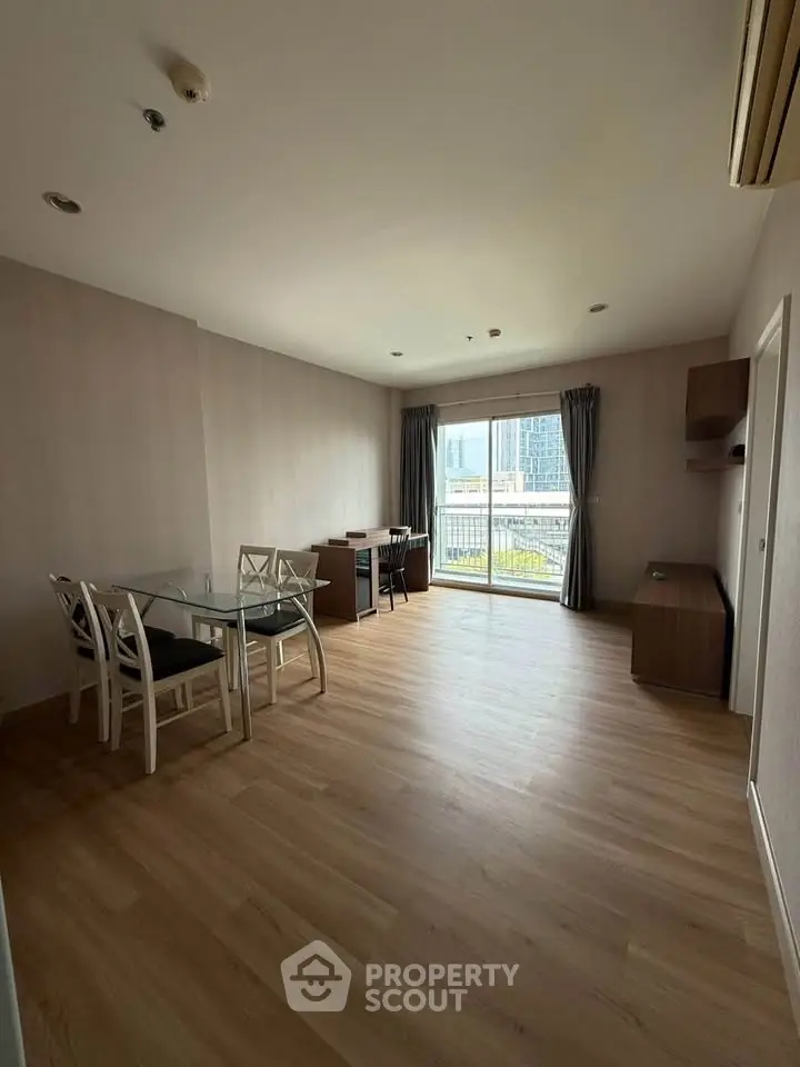 Spacious living room with wooden flooring and large window offering city view.